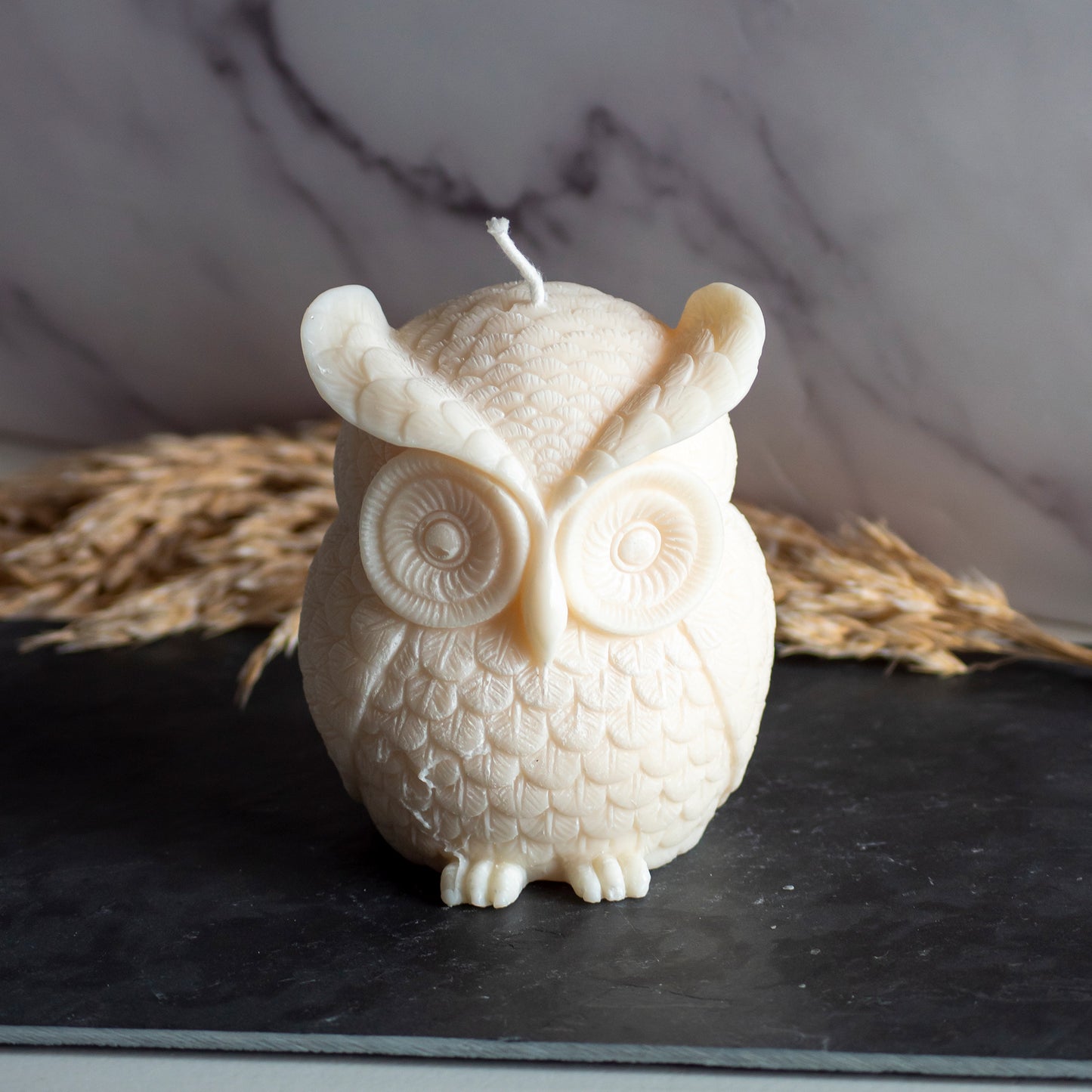 Beigekleurige Owl Glow kaars in rustige, natuurlijke setting