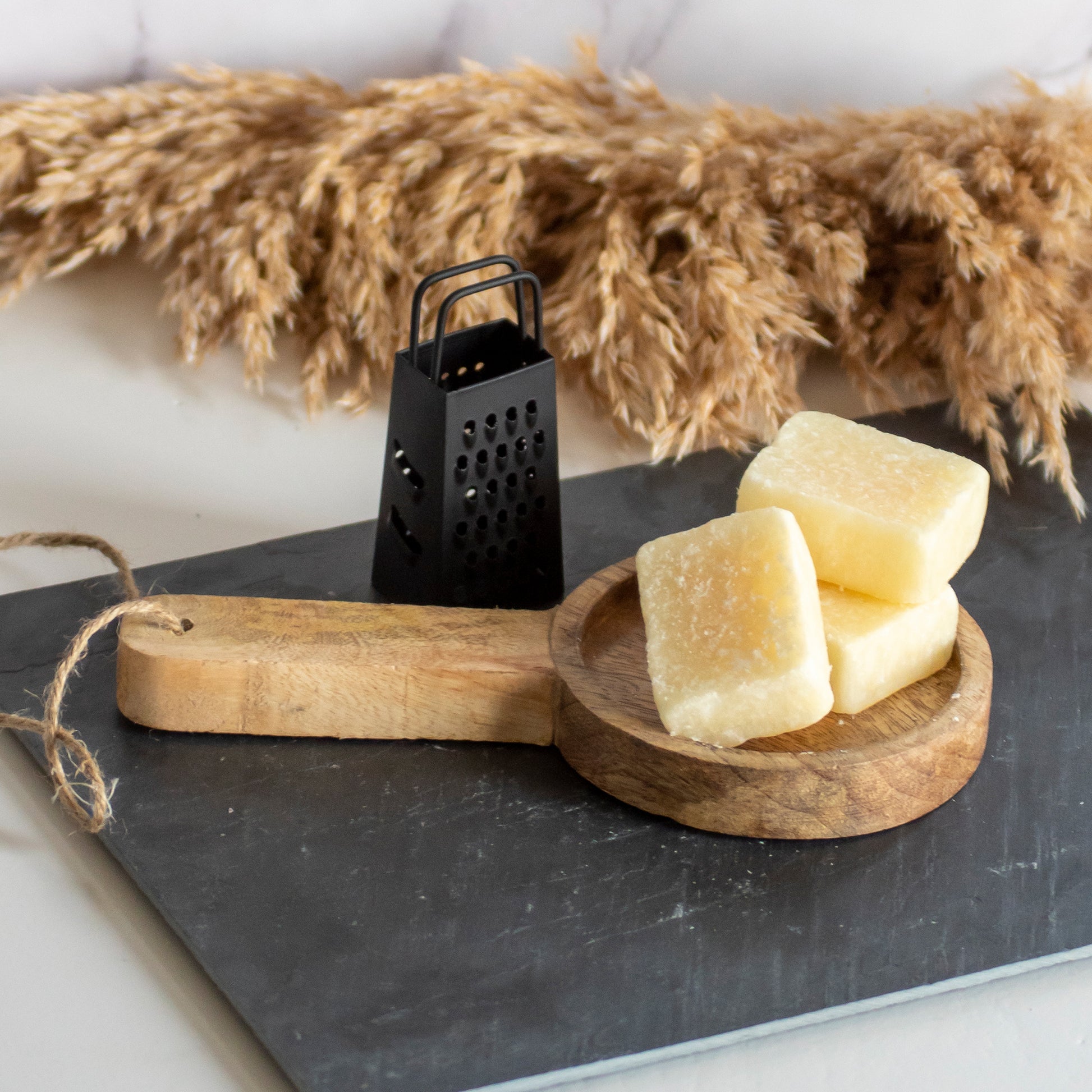 Houten plankje met drie vanille amberblokjes en een rasp op een stenen ondergrond