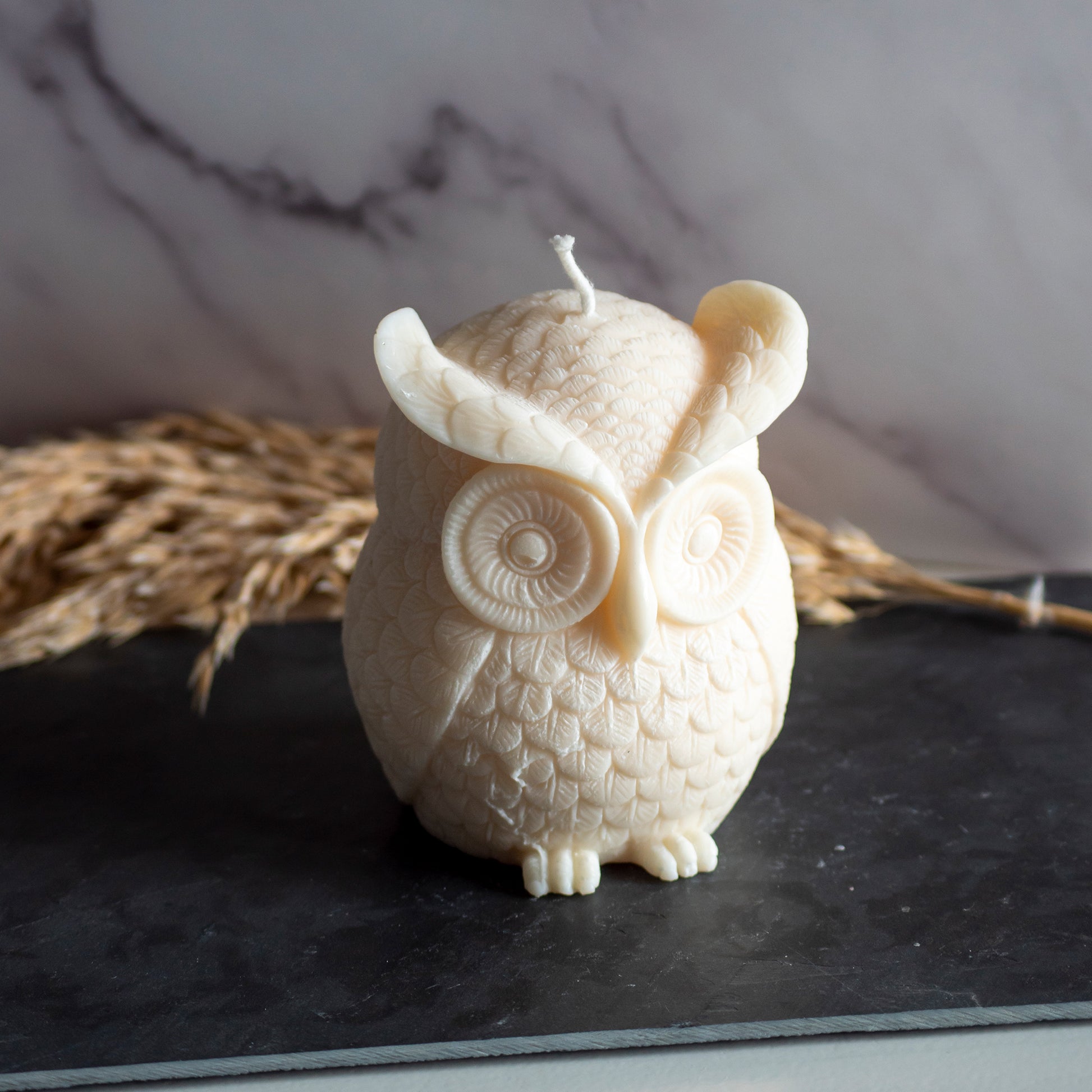 Beigekleurige Owl Glow kaars in rustige, natuurlijke setting