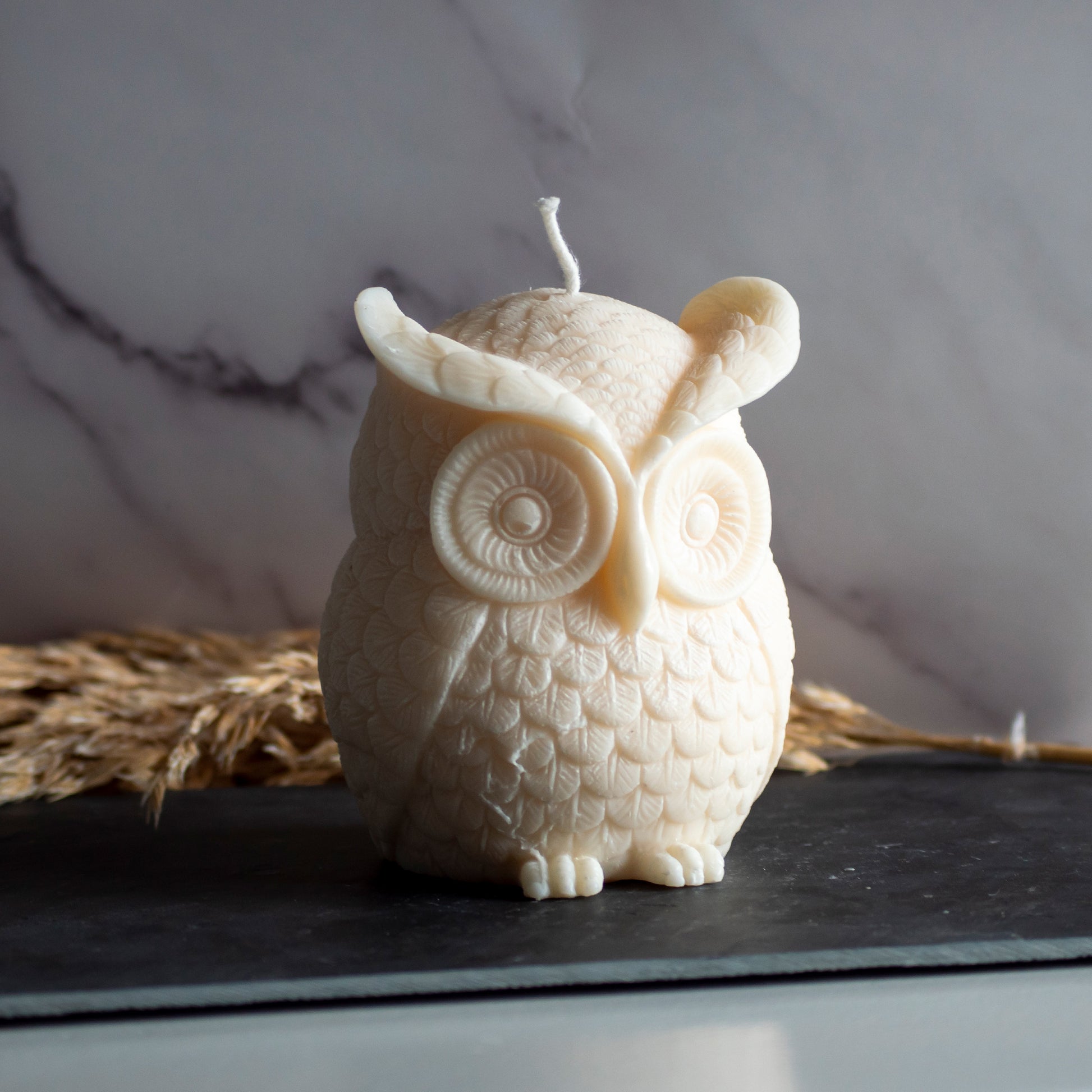 Beigekleurige Owl Glow kaars in rustige, natuurlijke setting