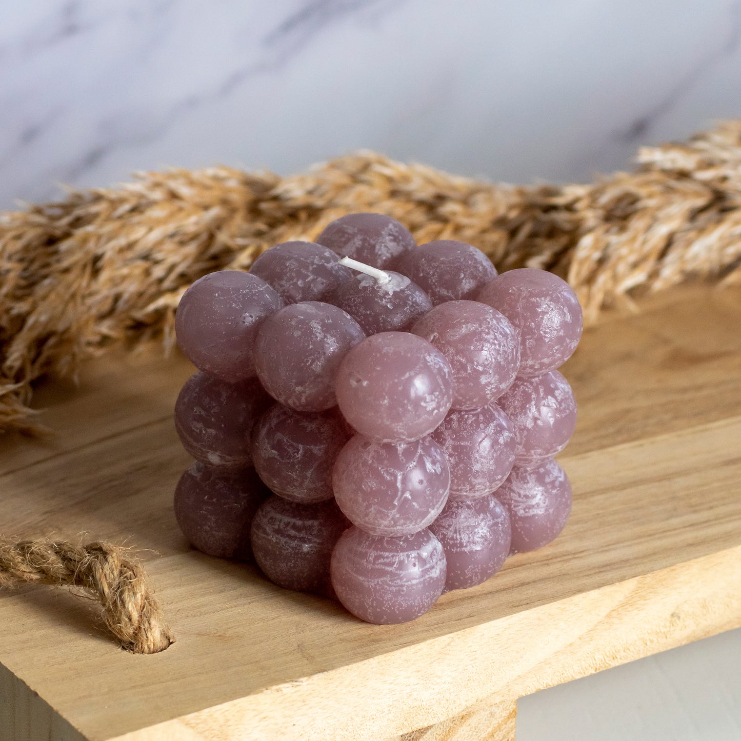 Bubbelkaars in kleur mauve op houten plank met pluimen als decoratie