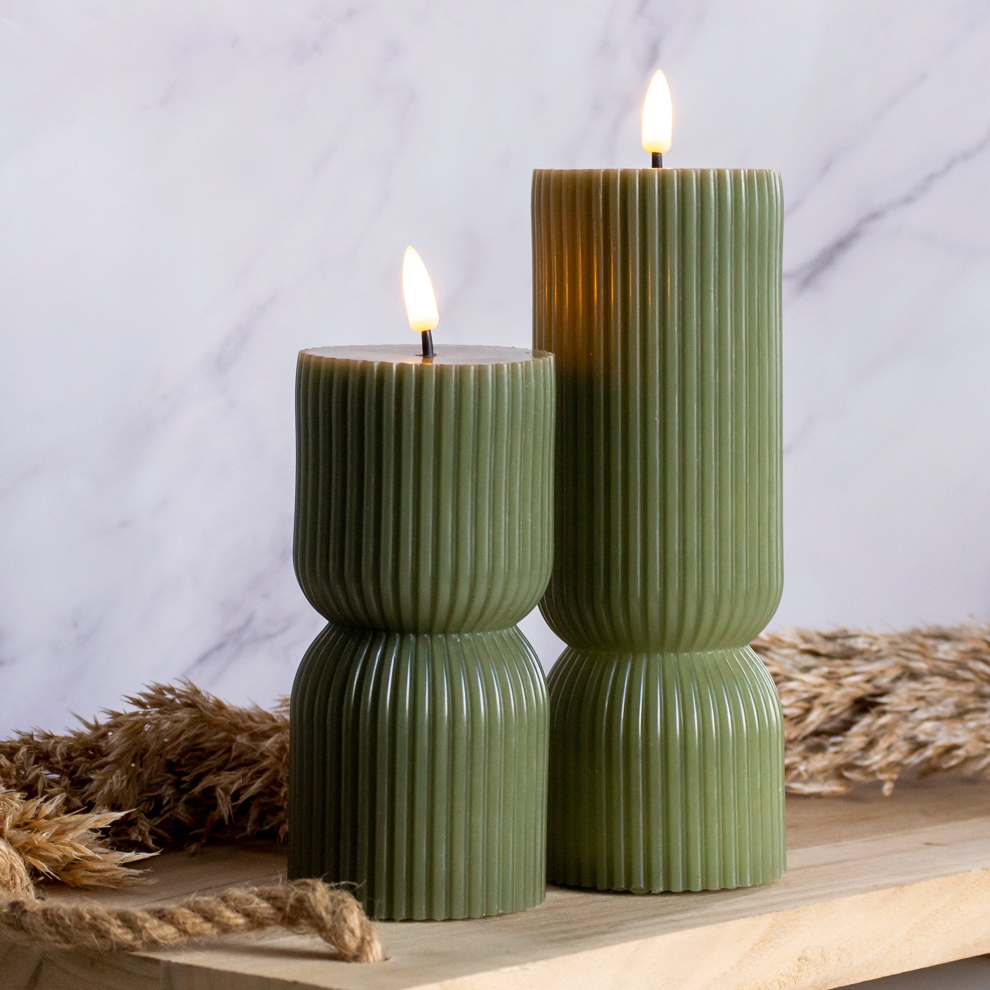 Hoge en lage LED kaarsen in groene kleur op houten plank met tarwe als decoratie
