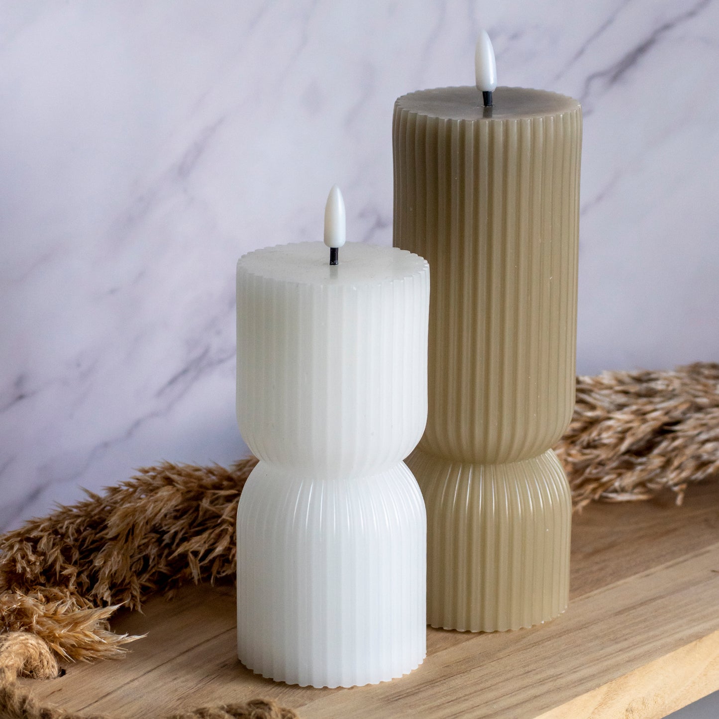 Hoge en lage LED kaarsen in wit en taupe op houten plank met tarwe als decoratie