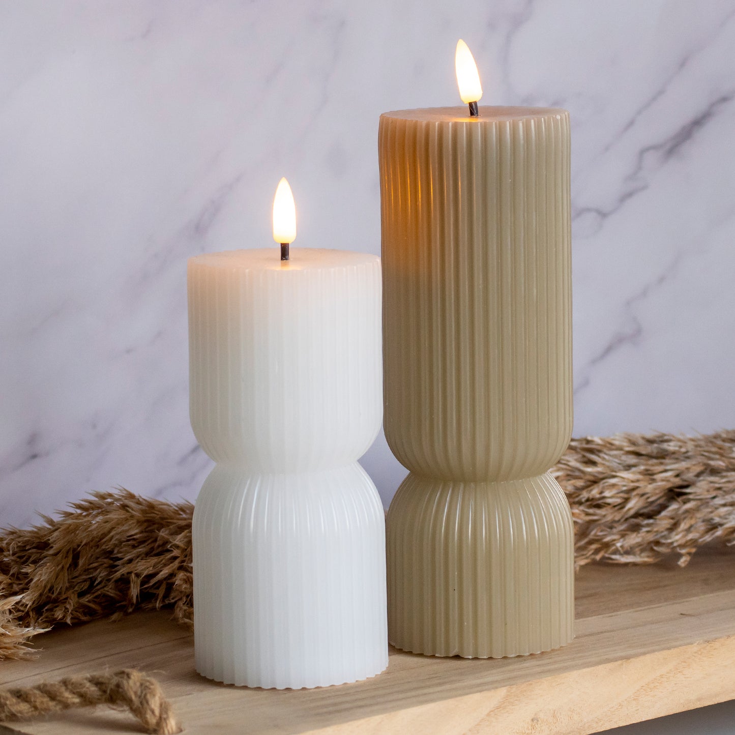 Hoge en lage LED kaarsen in wit en taupe op houten plank met tarwe als decoratie
