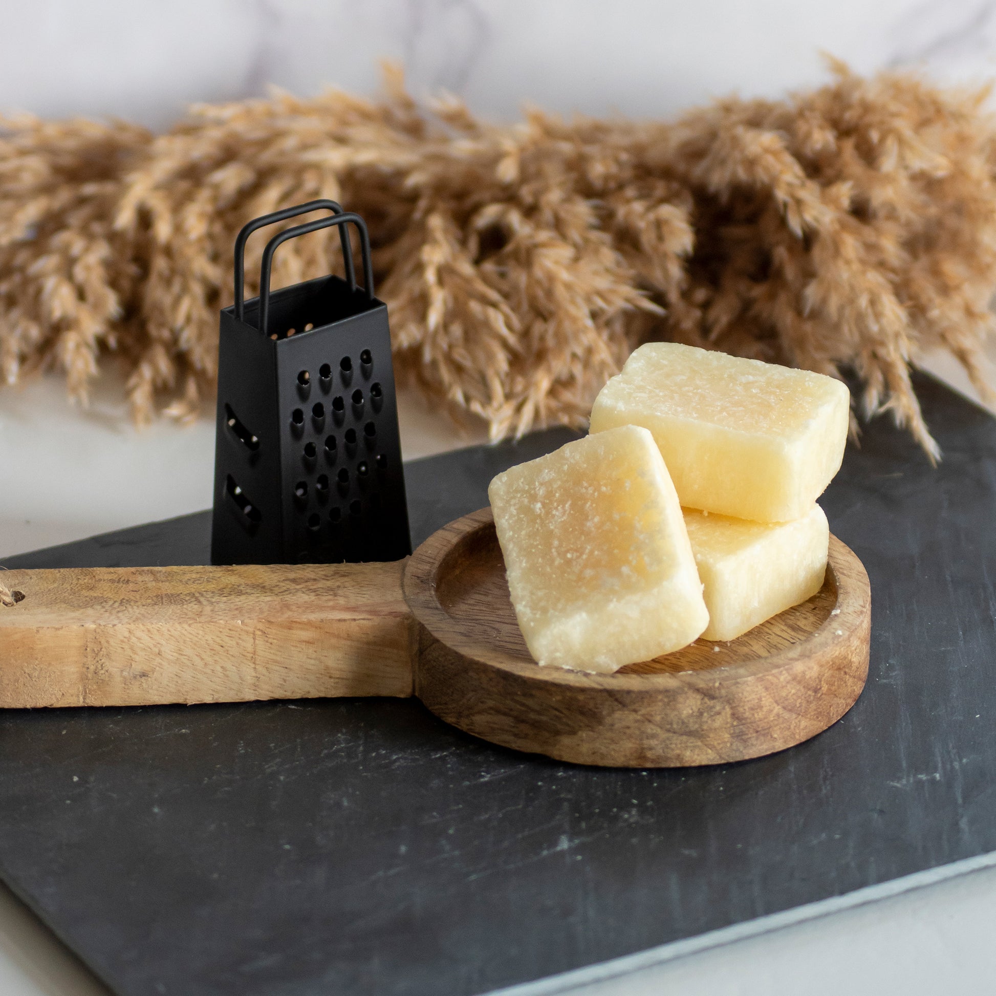 Rasp naast een houten plankje met drie vanille amberblokjes op een stenen ondergrond