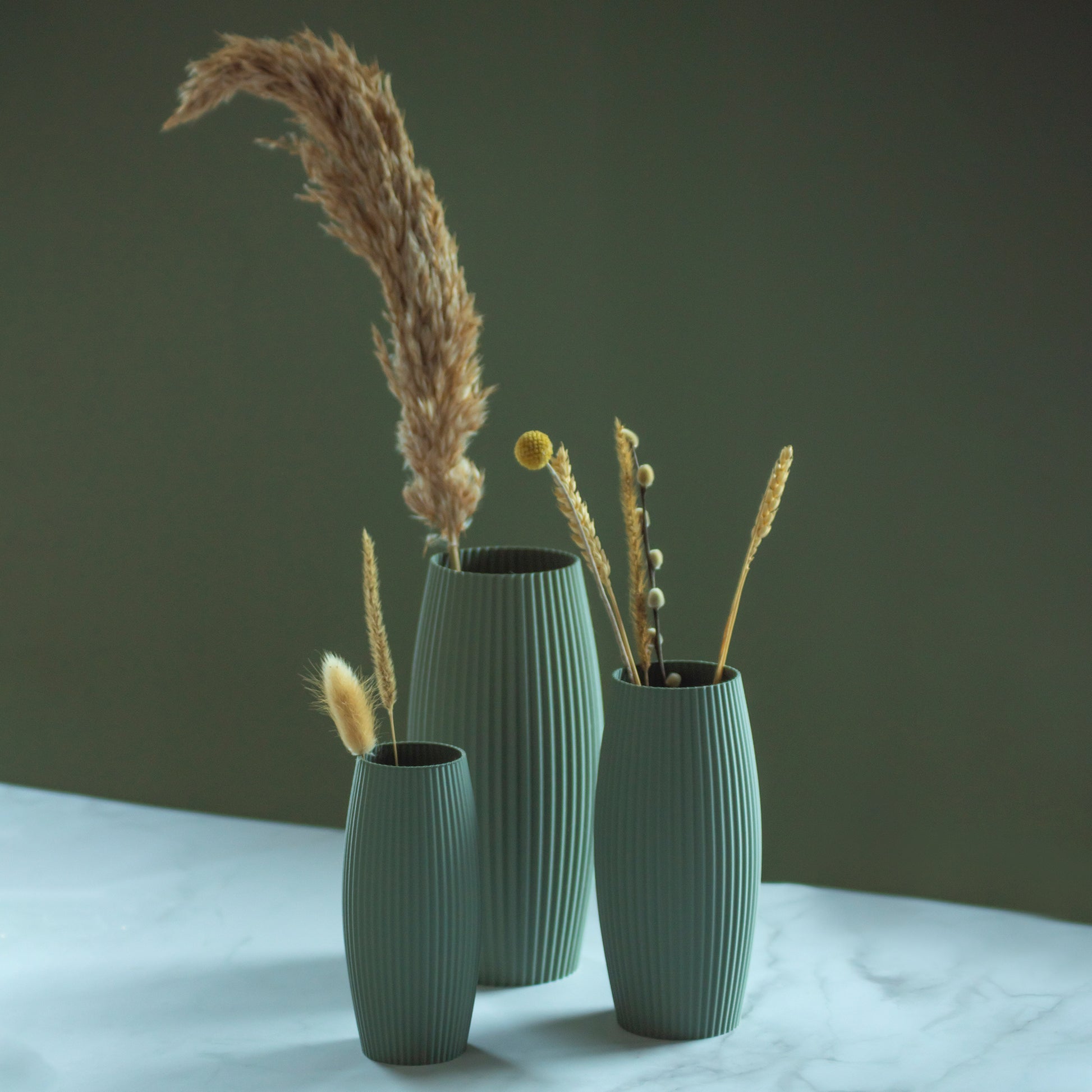 Olijfgroene vazen Nomi met droogbloemen op marmeren blad en groene achtergrond