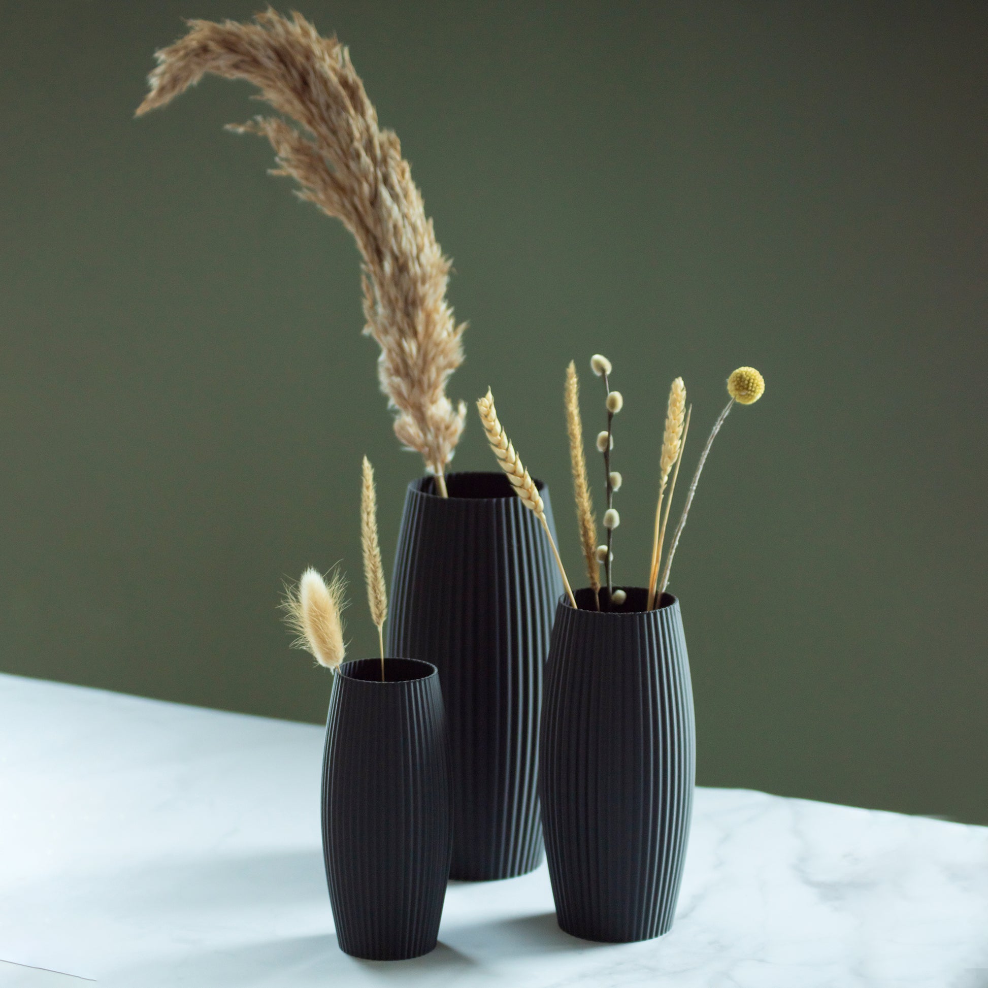 Zwarte vazen Nomi met droogbloemen op marmeren blad en groene achtergrond