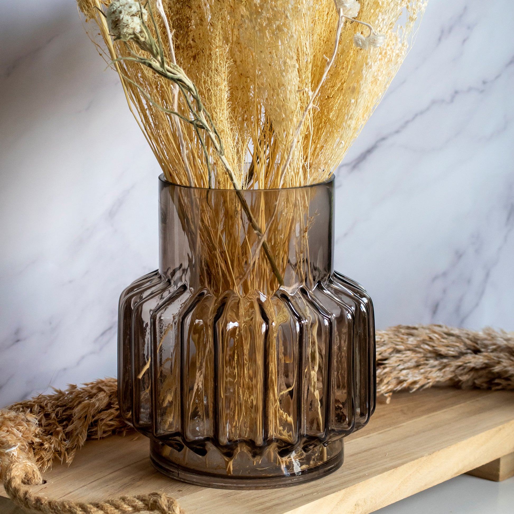 Grote bruine glazen vaas met droogbloemen op een houten plank