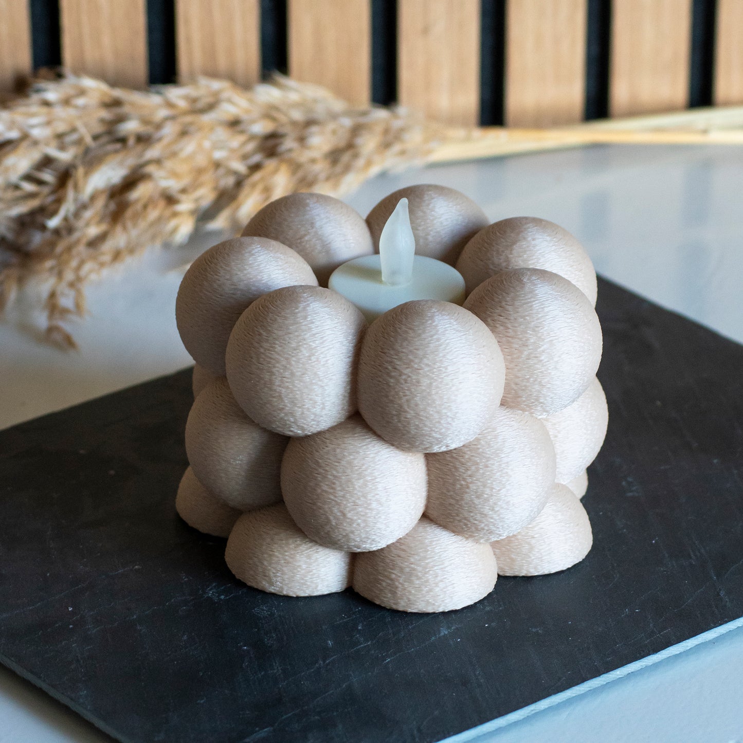 Waxinelichthouder met bubbelpatroon in kleur latte voor LED lichtjes op witte tafel en houten achtergrond